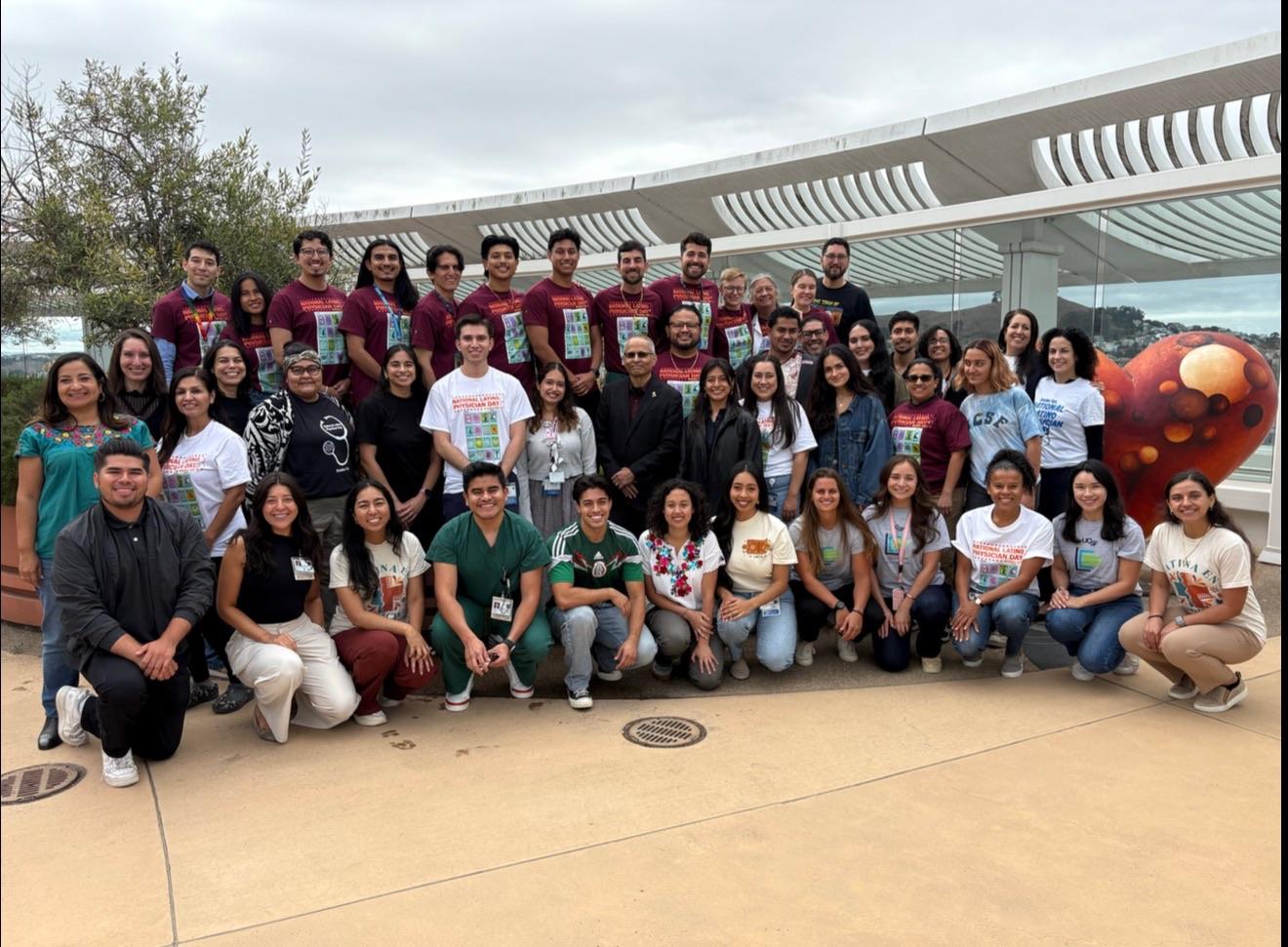Large group at National Latine Physician Day 2025 outdoors in front of a modern building with a heart sculpture.