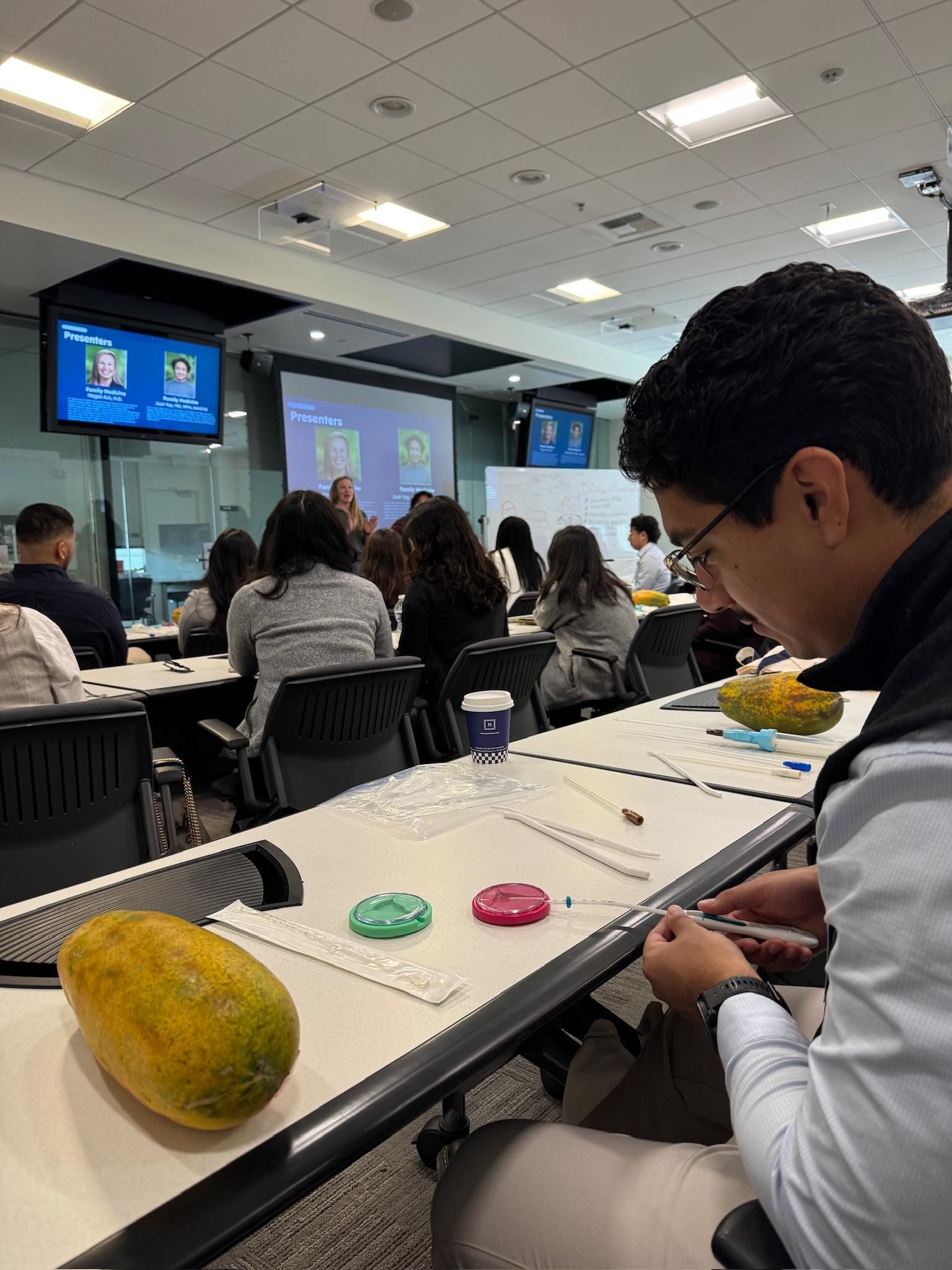 Students in a classroom watching a clinical demonstration on a papaya during a skills session.